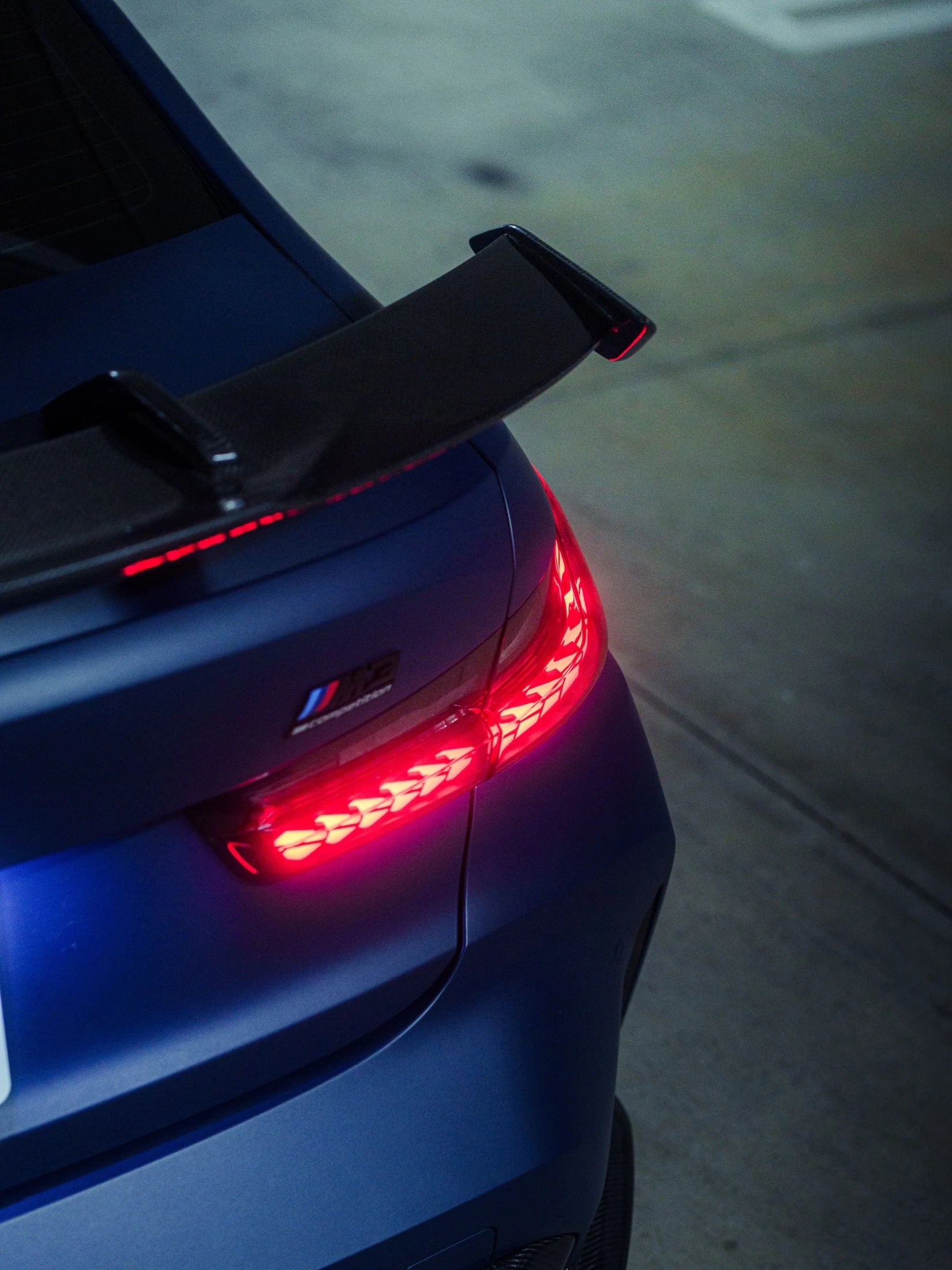 Illuminated rear light and carbon wing of a blue BMW M3